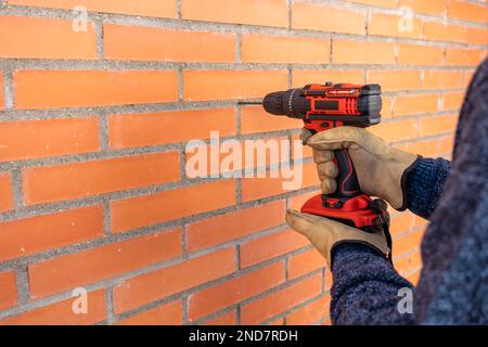 Foreuse avec batterie faisant des trous dans un mur de briques à l'extérieur. Banque D'Images