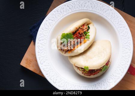 Concept alimentaire Buns Bao de bœuf bio ou Gua Bao faits maison dans une plaque en céramique blanche sur fond noir avec espace de copie Banque D'Images