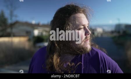 Un drôle de surpoids jeune homme secouant la tête avec les cheveux longs. Bonne personne libre sentant le vent à l'extérieur Banque D'Images