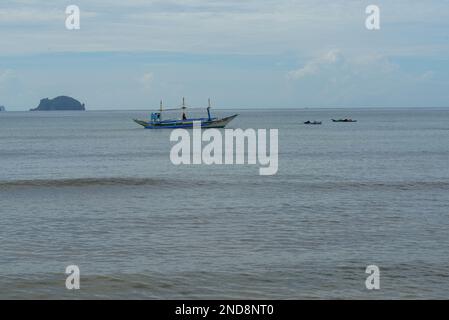 Cette photo capture l'essence des Philippines, avec un bateau traditionnel en bois qui navigue sur des eaux turquoise cristallines, entouré d'un vert luxuriant Banque D'Images