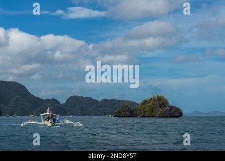 Cette photo capture l'essence des Philippines, avec un bateau traditionnel en bois qui navigue sur des eaux turquoise cristallines, entouré d'un vert luxuriant Banque D'Images