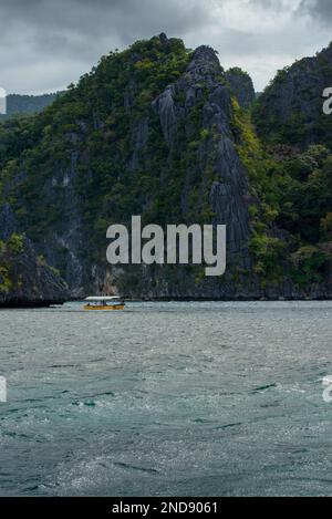 Cette photo capture l'essence des Philippines, avec un bateau traditionnel en bois qui navigue sur des eaux turquoise cristallines, entouré d'un vert luxuriant Banque D'Images