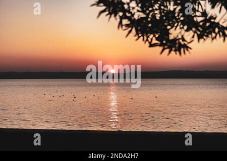 Magnifique coucher de soleil sur le magnifique lac de Garde en Italie, avec le soleil se reflétant sur l'eau calme et créant une atmosphère paisible. Parfait pour les Banque D'Images