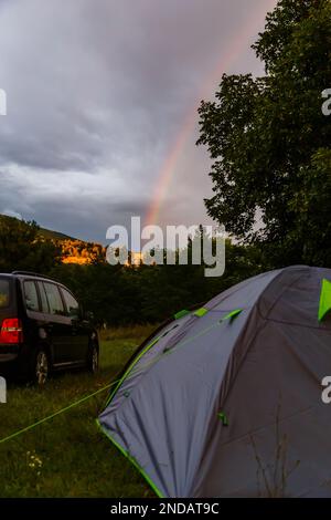 Un cliché vertical du bel arc-en-ciel brillant dans le ciel sombre derrière une tente et une voiture Banque D'Images