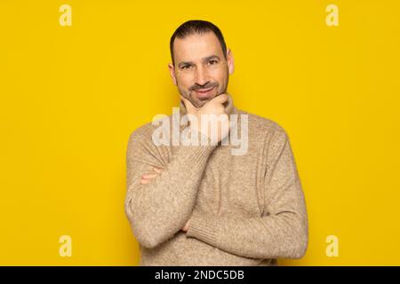 Solution au problème. L'homme hispanique barbu dans un turtleneck beige se débarrasse d'un problème, et. il regarde, fait une idée. arrière-plan jaune isolé. Banque D'Images