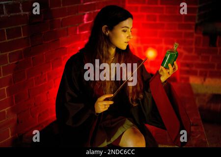 Jeune femme en peignoirs assis tenant le Wand et la bouteille de potion Magic Light émis par Wand | Rouge | Moody Banque D'Images