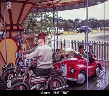 Les jeunes garçons font un tour de Merry-Go-Round (rond-point) à Christchurch, Dorset en 1962. Cette photo a été prise à partir de la diapositive d'origine. les voitures des années 1960 sont garées en arrière-plan. Banque D'Images