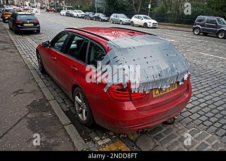 Voiture avec fenêtre arrière cassée patchée avec ruban adhésif dans la nouvelle ville d'Édimbourg. Banque D'Images