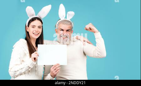 Le couple de Pâques vêtu de costume tenant un tableau blanc vierge pour votre texte.Bannière avec un couple de lapins drôle, espace de copie. Banque D'Images