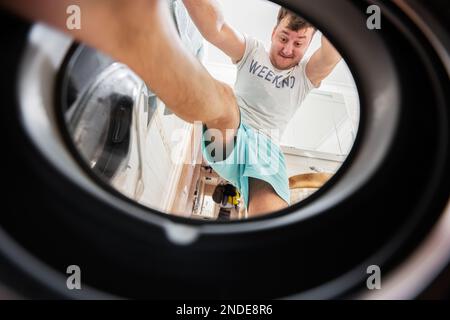 Vue sur l'homme depuis le lave-linge à l'intérieur. Homme fait la routine quotidienne. Monte à l'intérieur, poussant et pressant le linge avec ses pieds. Banque D'Images