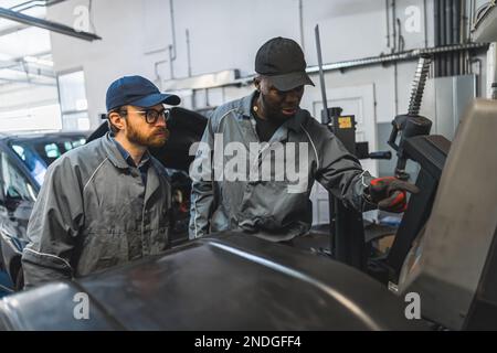 deux mécaniciens professionnels travaillant à un poste de réparation de voiture, plan moyen, atelier de réparation concept. Photo de haute qualité Banque D'Images