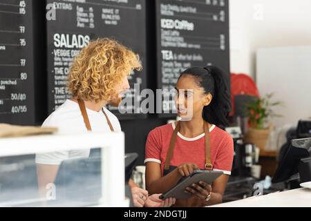 Joyeux baristas hommes et femmes divers portant des tabliers et utilisant une tablette dans le café. Café, temps libre et concept de ville. Banque D'Images