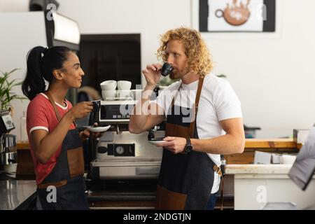Joyeux baristas hommes et femmes portant des tabliers et buvant du café dans le café. Café, temps libre et concept de ville. Banque D'Images