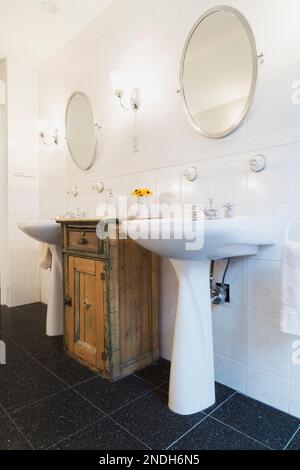 Son piédestal s'enfonce entre la vieille vanité en bois dans la salle de bain principale avec sol en carrelage de granit noir à l'étage à l'intérieur de la vieille maison victorienne de 1900. Banque D'Images