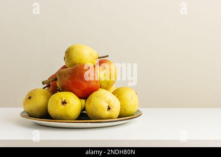 Une assiette pleine à débordante de délicieuses poires mûres sur une étagère blanche Banque D'Images