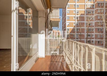 Une terrasse d'une maison avec une main courante en métal blanc et de grandes fenêtres en verre et en aluminium menant à un salon vide et une vue sur un pâté de maisons courty Banque D'Images