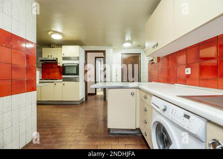 Cuisine équipée d'armoires crème avec comptoir blanc avec porte d'accès en bois sombre, carrelage rouge et blanc sur les murs et vieux planchers bruns Banque D'Images