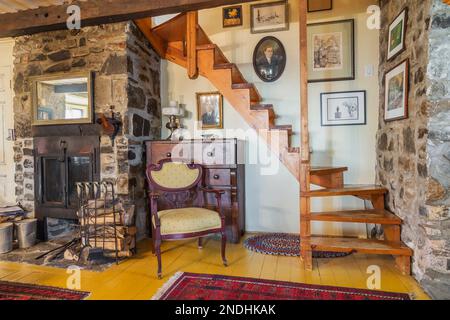 Cheminée en pierre des champs et fauteuil rembourré antique à côté d'une commode en bois et escalier en bois de pin tournant menant à l'étage supérieur dans le salon. Banque D'Images