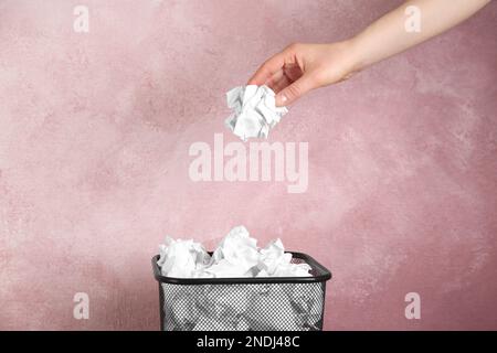 Femme jetant une boule de papier froissé dans le panier sur fond rose, gros plan Banque D'Images