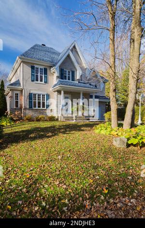 Façade de maison de style cottage en brique et vinyle brun clair avec garniture bleue et toit en bardeaux d'asphalte en automne. Banque D'Images