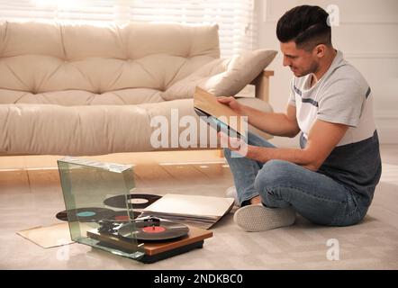Homme avec un disque en vinyle près de la platine dans le salon Banque D'Images