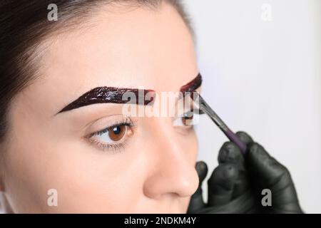 Esthéticienne appliquant la teinte pendant la procédure de correction des sourcils sur fond clair, gros plan Banque D'Images