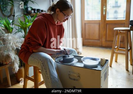 Concentré artisan travaillant minutieusement à la fabrication de produits d'argile sur la roue de potiers en atelier. Banque D'Images