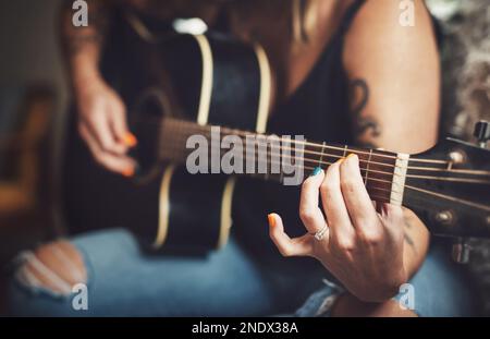 Dites-le avec des cordes. une femme méconnaissable jouant une guitare à la maison. Banque D'Images