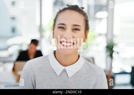 Je suis confiant dans mon travail. Portrait court d'une jeune femme d'affaires attirante debout seule au bureau et souriant à l'appareil photo. Banque D'Images