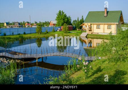 Un chalet en bois avec un belvédère se trouve dans un jardin près d'un étang avec un pont et des fleurs. Banque D'Images