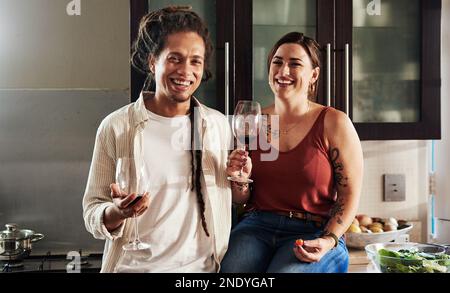 Envoyez plus de vin s'il vous plaît. Portrait d'un jeune couple gai appréciant un verre de vin ensemble tout en se tenant dans la cuisine à la maison. Banque D'Images