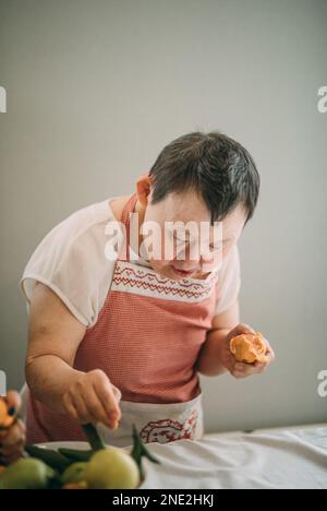 la femme âgée atteinte du syndrome de down étudie dans les peaux de cuisine tangerines Banque D'Images