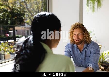 Joyeux couple varié assis à table et parlant au café. Café, temps libre et concept de ville. Banque D'Images