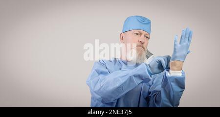 Le médecin traitant des maladies infectieuses âgées dans une combinaison de protection bleue met des gants en caoutchouc. Banque D'Images