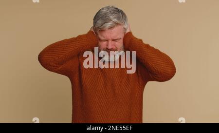 Je ne veux pas entendre et écouter. Frustré agacé agacé homme d'âge moyen couvrant les oreilles gestante non, évitant les conseils ignorant bruit désagréable voix fortes. Homme mature senior sur fond beige Banque D'Images