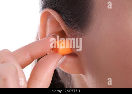 Jeune femme insérant un bouchon d'oreille en mousse sur fond blanc, gros plan Banque D'Images