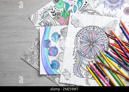 Pages de coloriage antistress et crayons sur table en bois clair, plat Banque D'Images