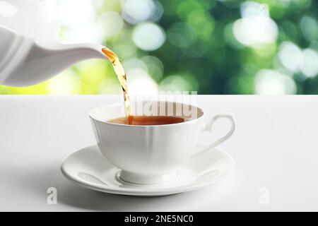 Verser le thé dans une tasse sur une table blanche sur un fond flou Banque D'Images