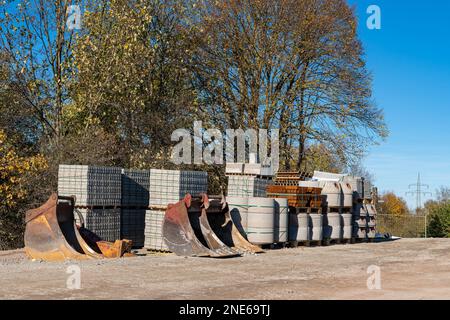 Chantier de construction avec matériaux en béton et pavés. Godets de pelle hydraulique au premier plan. Banque D'Images