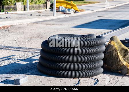 Tuyau ondulé noir enroulé dans une bobine sur un chantier de construction. Construction de trottoirs et de routes fraîchement pavés. Banque D'Images