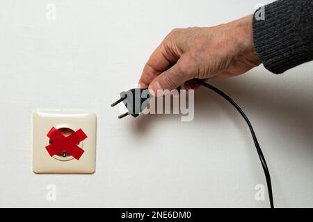 La main d'un homme essaie de brancher une fiche dans une prise électrique scellée avec du ruban électrique rouge. Crise énergétique mondiale. Gros plan. Banque D'Images