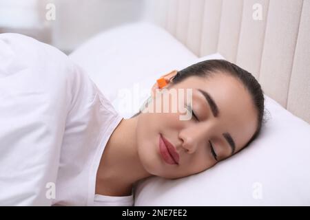 Jeune femme avec des bouchons d'oreilles en mousse dormant dans le lit Banque D'Images