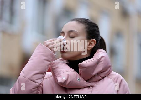 Femme malade avec des mouchoirs en papier éternuant à l'extérieur Banque D'Images