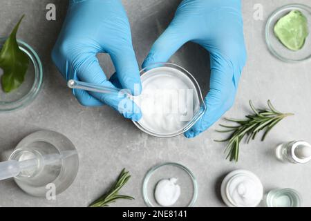 Scientifique faisant des produits cosmétiques à la table grise, vue de dessus Banque D'Images