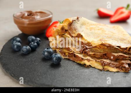 Crêpes fines délicieuses avec tartinade au chocolat et bleuets sur table grise, en gros plan Banque D'Images