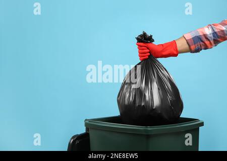 Homme jetant un sac poubelle dans la poubelle sur fond bleu clair, gros plan. Espace pour le texte Banque D'Images