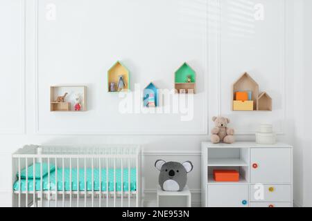 Lit de bébé confortable près du mur avec étagères colorées dans la chambre de bébé. Design intérieur Banque D'Images