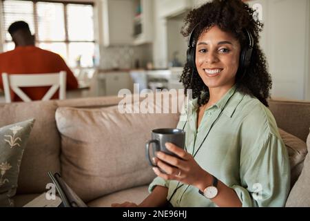 Femme souriante qui boit du café et regarde une vidéo sur une tablette à la maison Banque D'Images