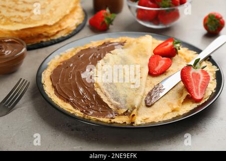 Crêpes fines délicieuses avec tartiner au chocolat et framboises sur table grise, en gros plan Banque D'Images