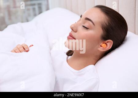 Jeune femme avec des bouchons d'oreilles en mousse dormant dans le lit Banque D'Images